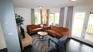 A living room with two sofas, a coffee table, a TV, and a plant. - Bungalow by Water With Sauna in South Holland (Simonshaven)