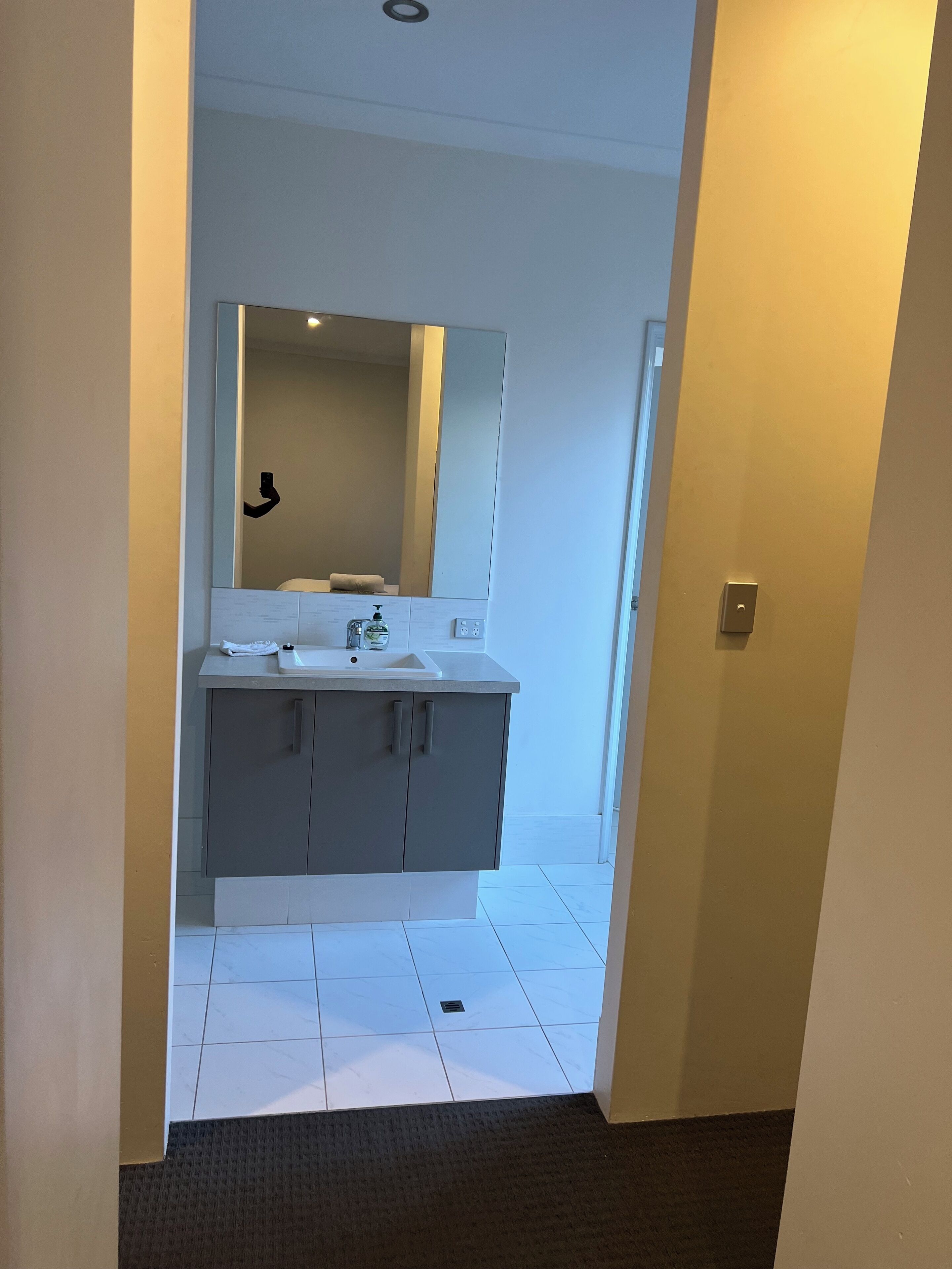 A modern bathroom with a large mirror, grey cabinets, and a white sink.