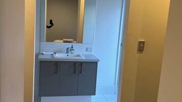 A modern bathroom with a large mirror, grey cabinets, and a white sink.
