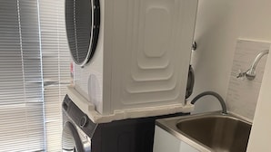 Une petite buanderie équipée d’un lave-linge et d’un sèche-linge à chargement frontal, d’un évier et d’un sol carrelé.