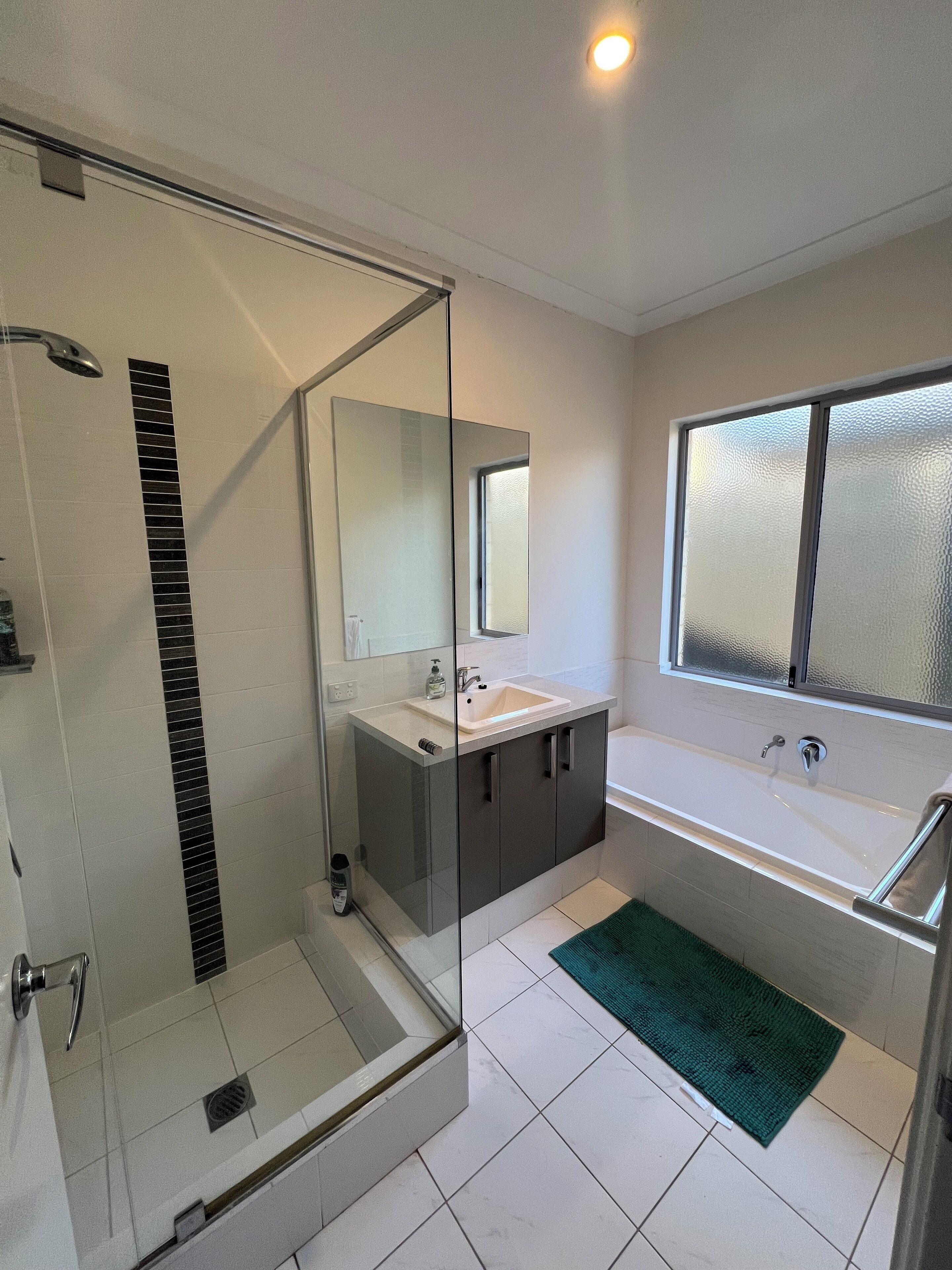Un bany modern amb dutxa de vidre, un mirall gran, un lavabo amb rentapès i una banyera.