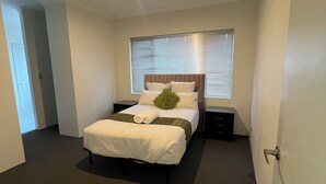 Une chambre d’hôtel moderne avec un grand lit, une table de chevet et une fenêtre avec des stores.