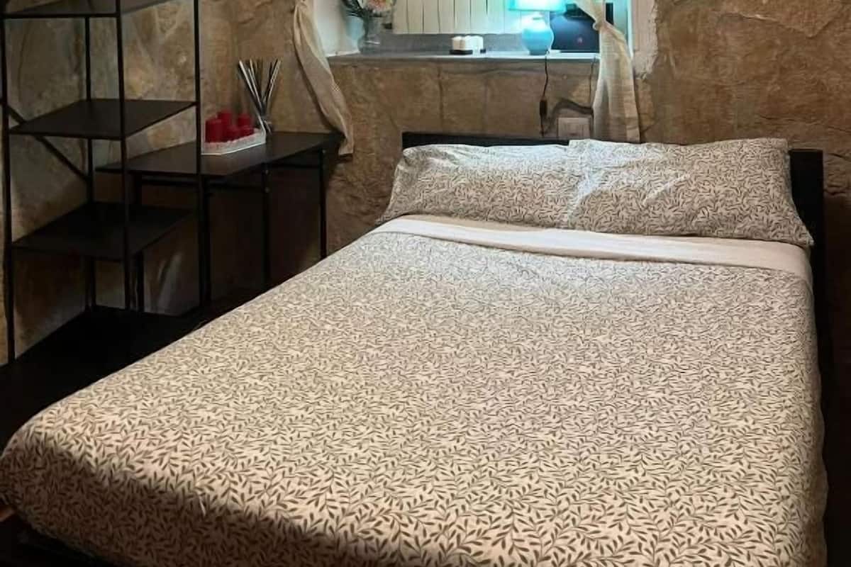 Un dormitorio con cama, mesita de noche, lámpara y ventana con cortinas.