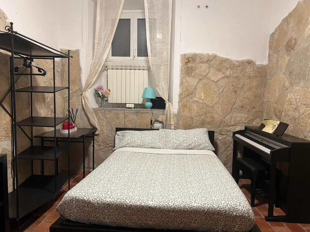 A bedroom with a bed, a piano, a shelf unit, and a window with curtains.