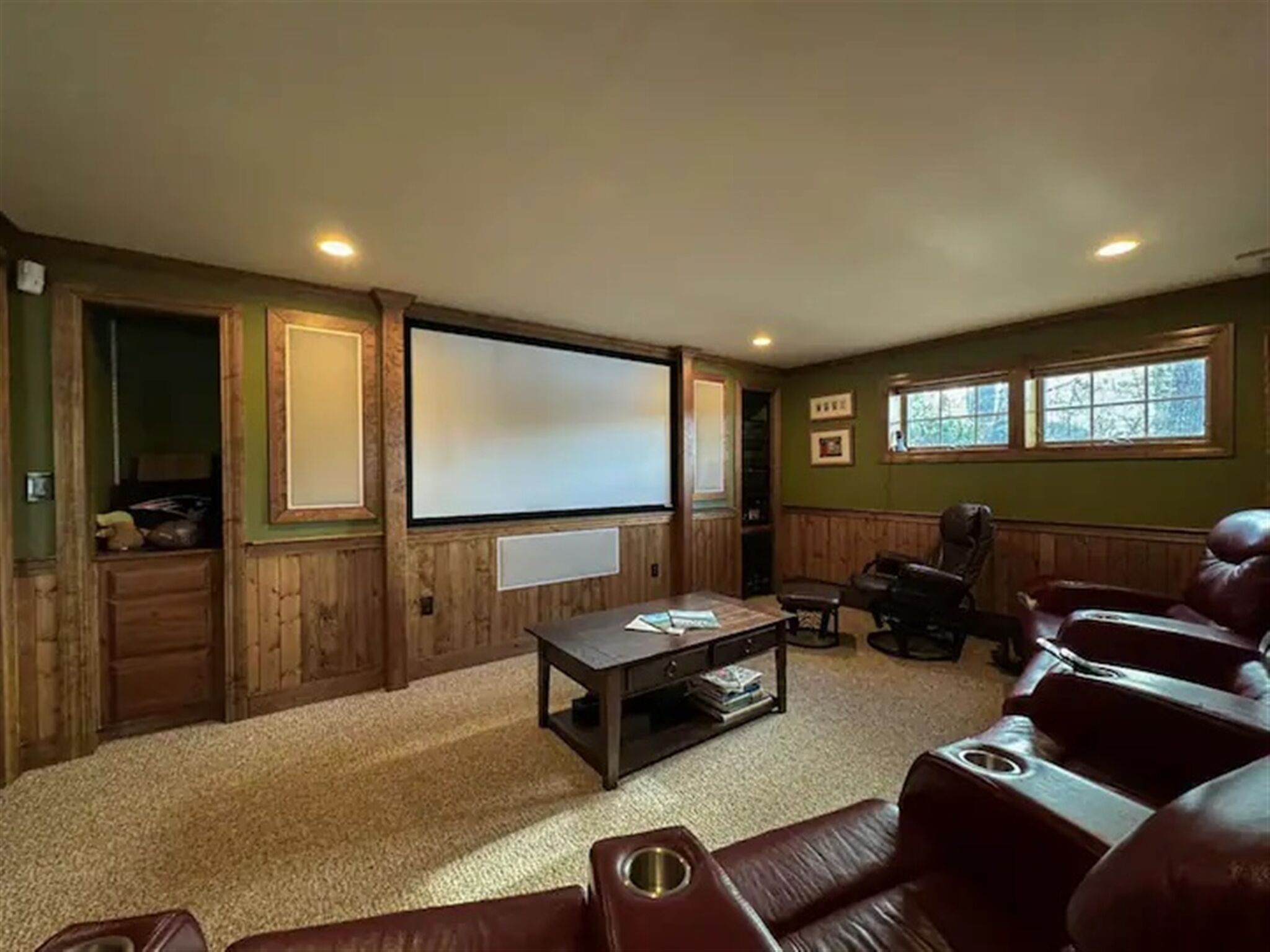 A home theater room with a large screen, leather recliners, and a small coffee table.