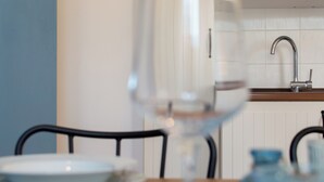 A dining table with a plate and a glass, a blue vase, and a kitchen area with a sink and cabinets in the background.