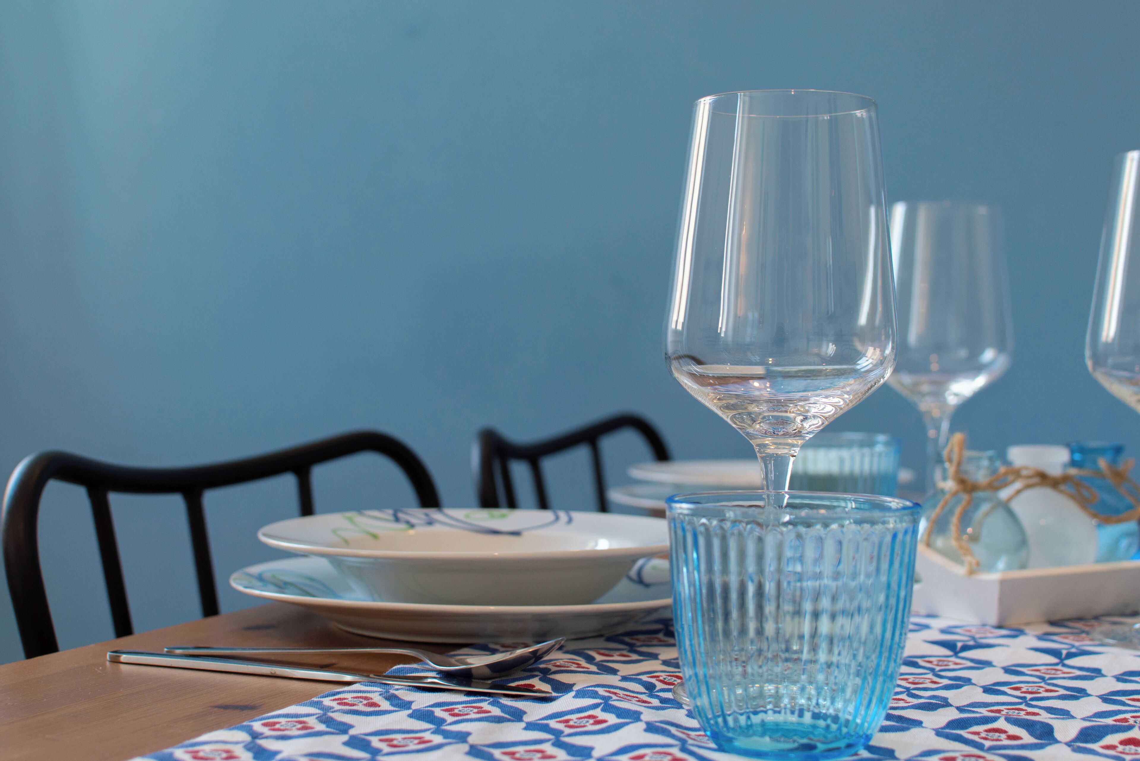 A dining table with a blue tablecloth, a wine glass, and a water glass.