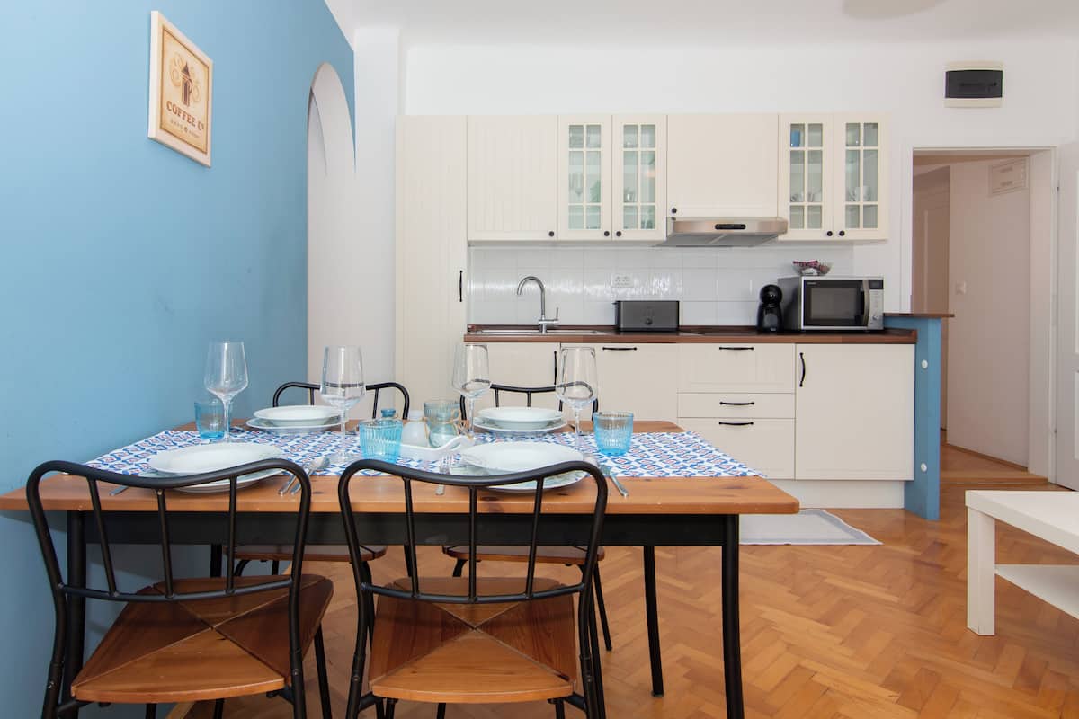 A dining area with a table set for four, a kitchen in the background, and a blue wall.