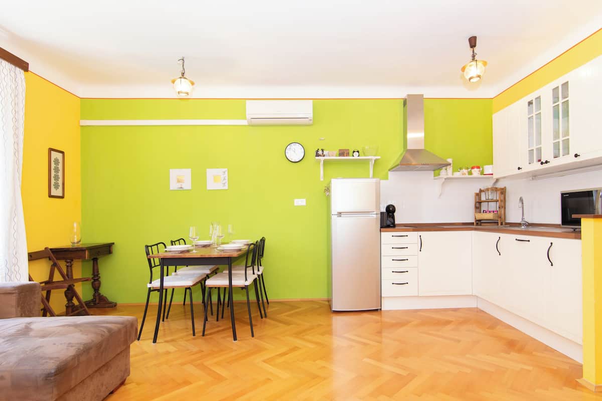 A compact kitchen with a dining area, featuring a wooden table set for four, a refrigerator, and a microwave.