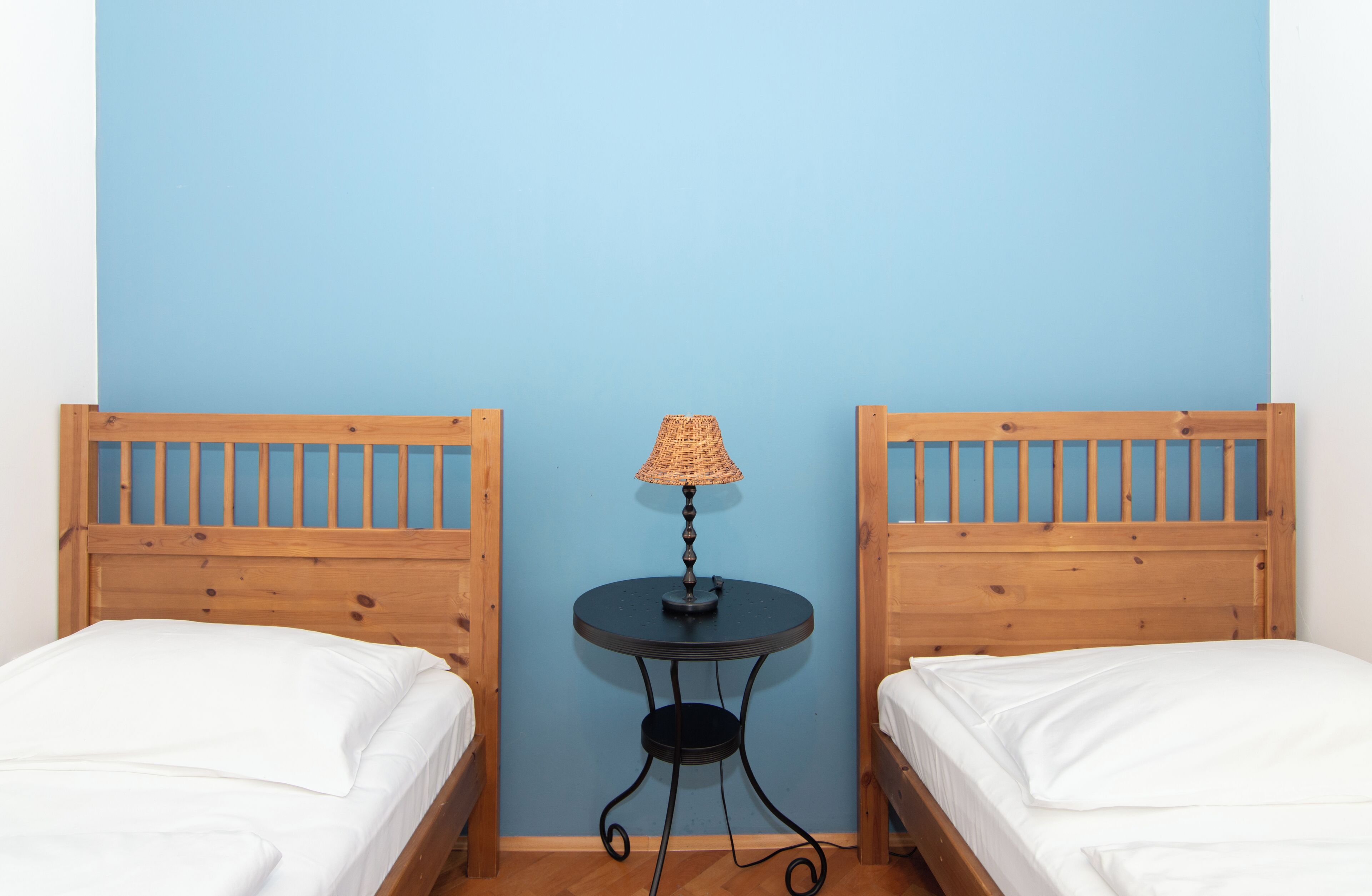 A room with two wooden beds, a small round table with a lamp, and a blue wall.