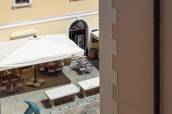 An outdoor patio area with tables and chairs, a large umbrella, and a building entrance. - Mare & Sole Apartments (Piran)