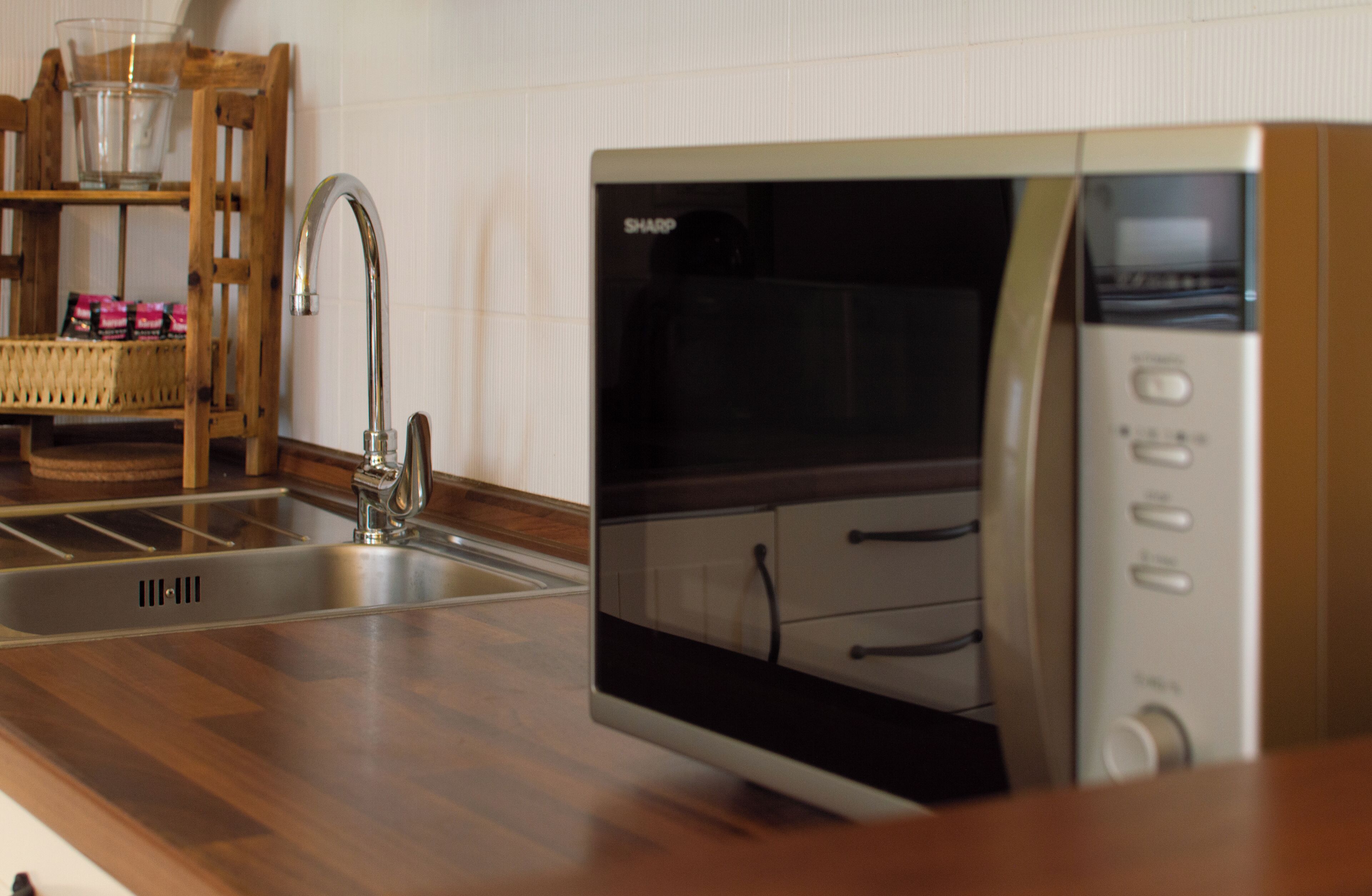 A kitchen with a stainless steel sink, a microwave, and a wooden chair with a basket.