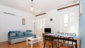 A living room with a sofa, dining table, chairs, and a TV.