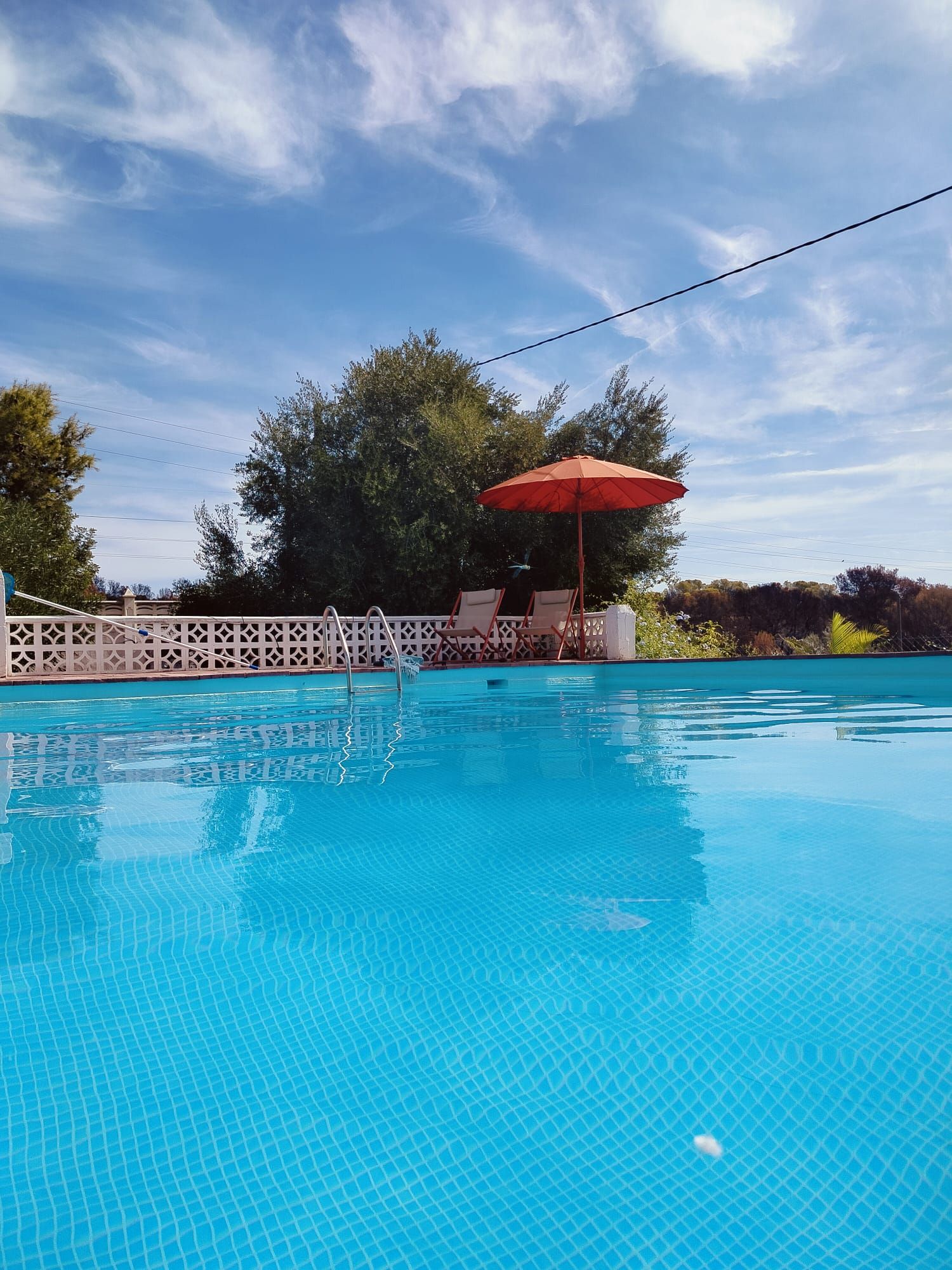 Una piscina amb una superfície d'aigua blava i cristal·lina, envoltada d'una tanca blanca amb disseny de reixeta.