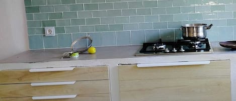 Une cuisine équipée d’une cuisinière à gaz, avec une casserole sur le brûleur et un crédence recouverte de carreaux verts.