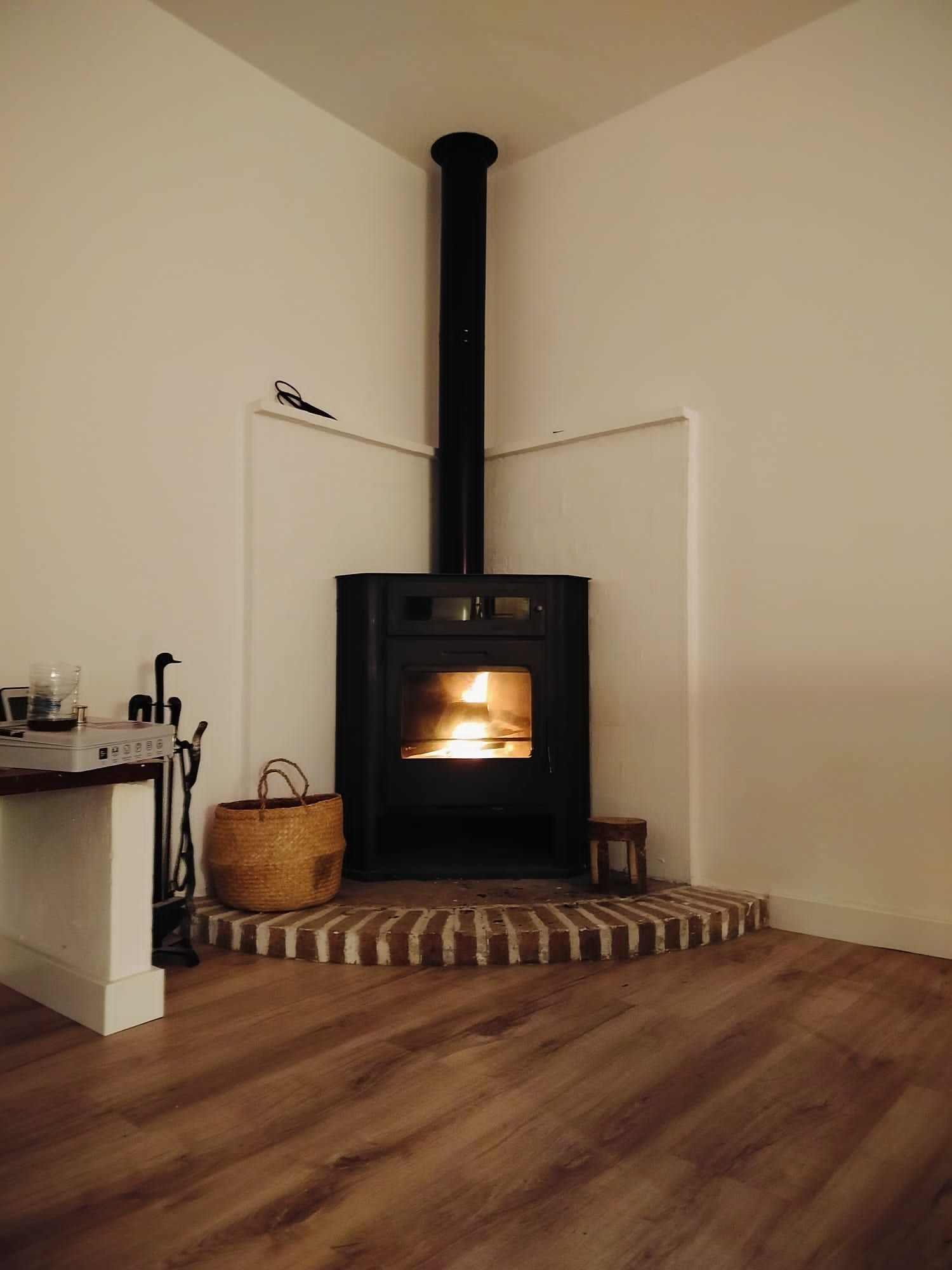 A room with a wood-burning stove, a small table with a basket, and a chair.