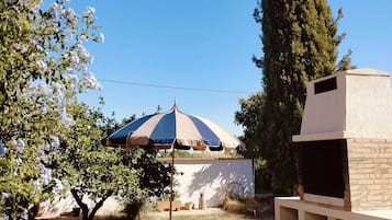A backyard with a barbecue grill, a tree, and a patio umbrella.