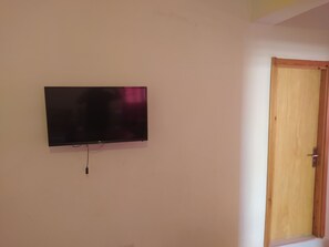Een kamer met een tv aan de muur, een houten deur en een wit plafond.