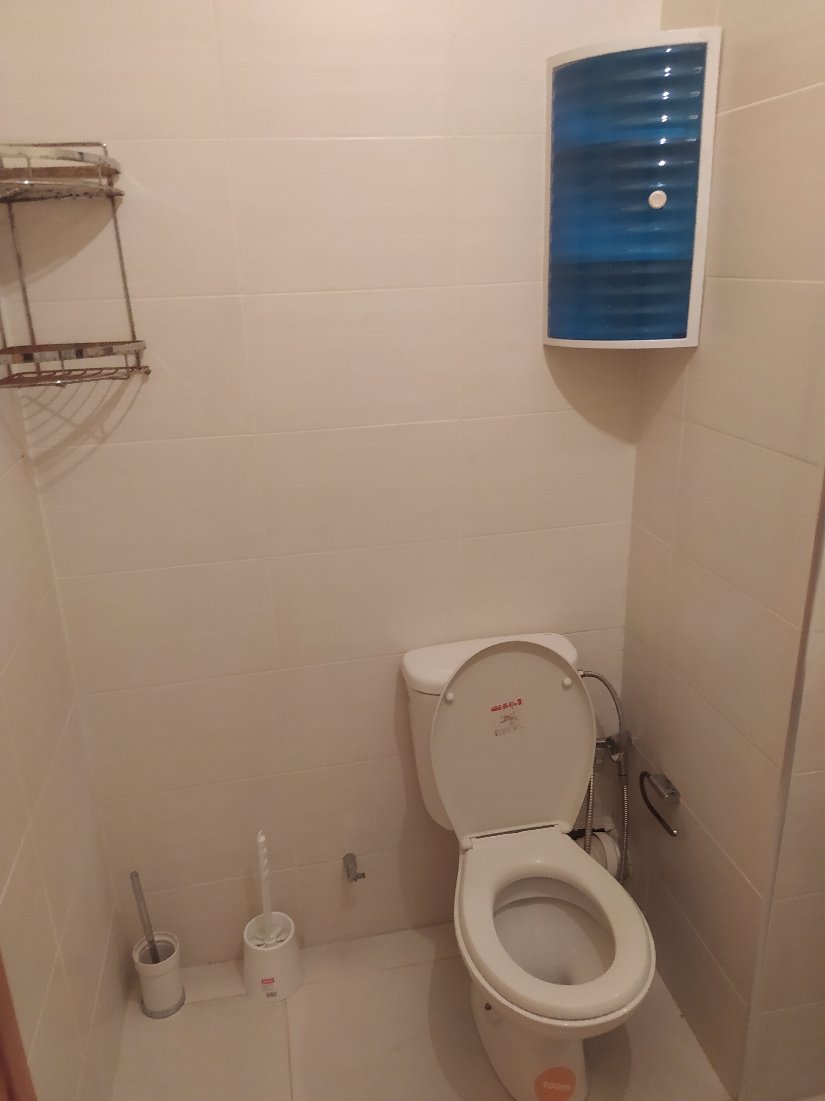 A small bathroom with a toilet, a hand dryer, and a blue soap dispenser on the wall.