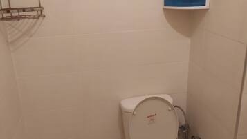 A small bathroom with a toilet, a hand dryer, and a blue soap dispenser on the wall.