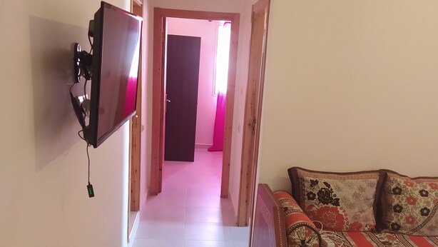 A hallway with a TV mounted on the wall, leading to a room with a sofa and patterned cushions. - Nice apartment in marakech, for a good stay  (Marakech)