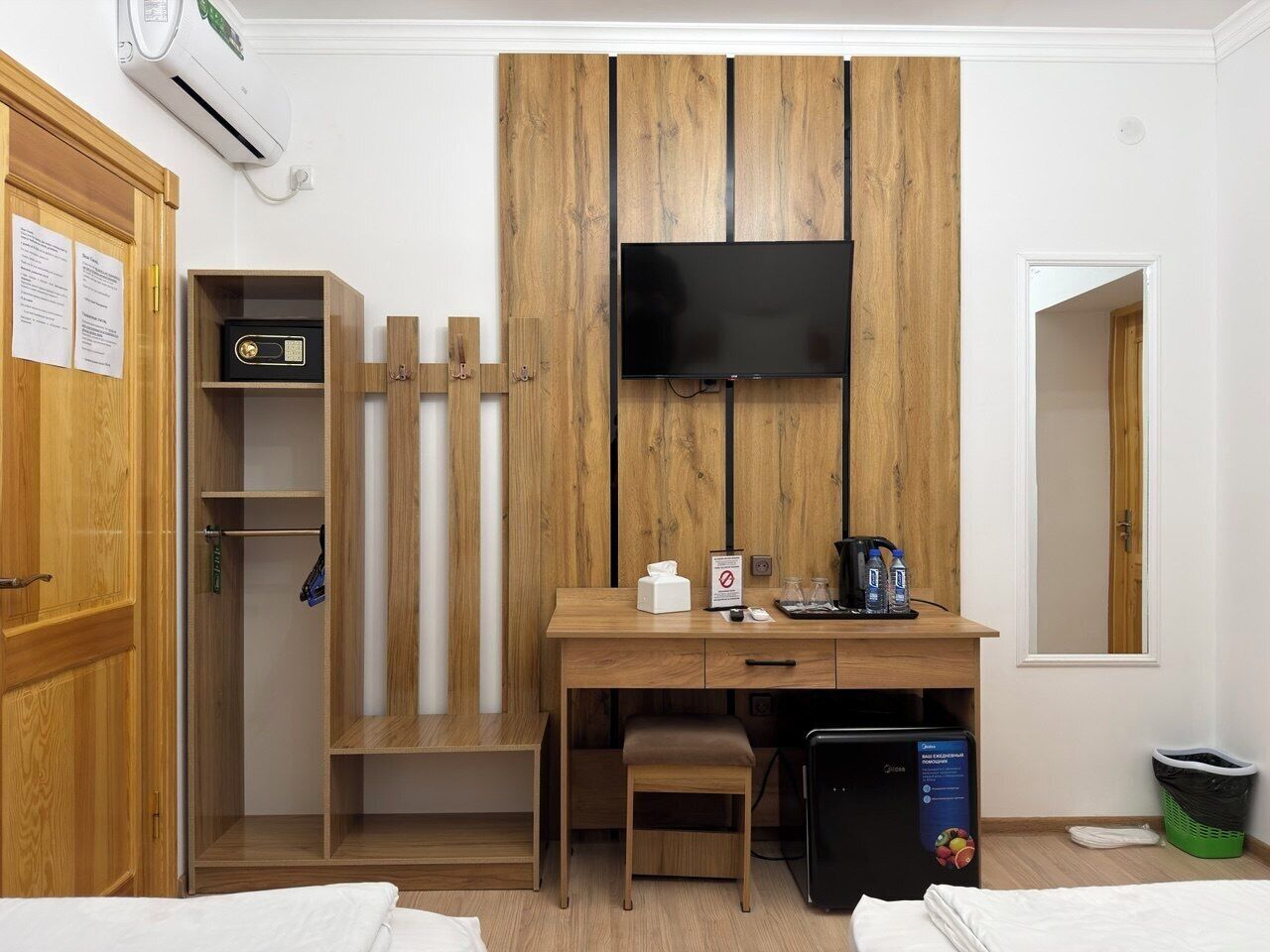 Habitación de hotel con armario de madera, un escritorio con televisor de pantalla plana, un taburete pequeño, un cesto de basura y una lavadora.
