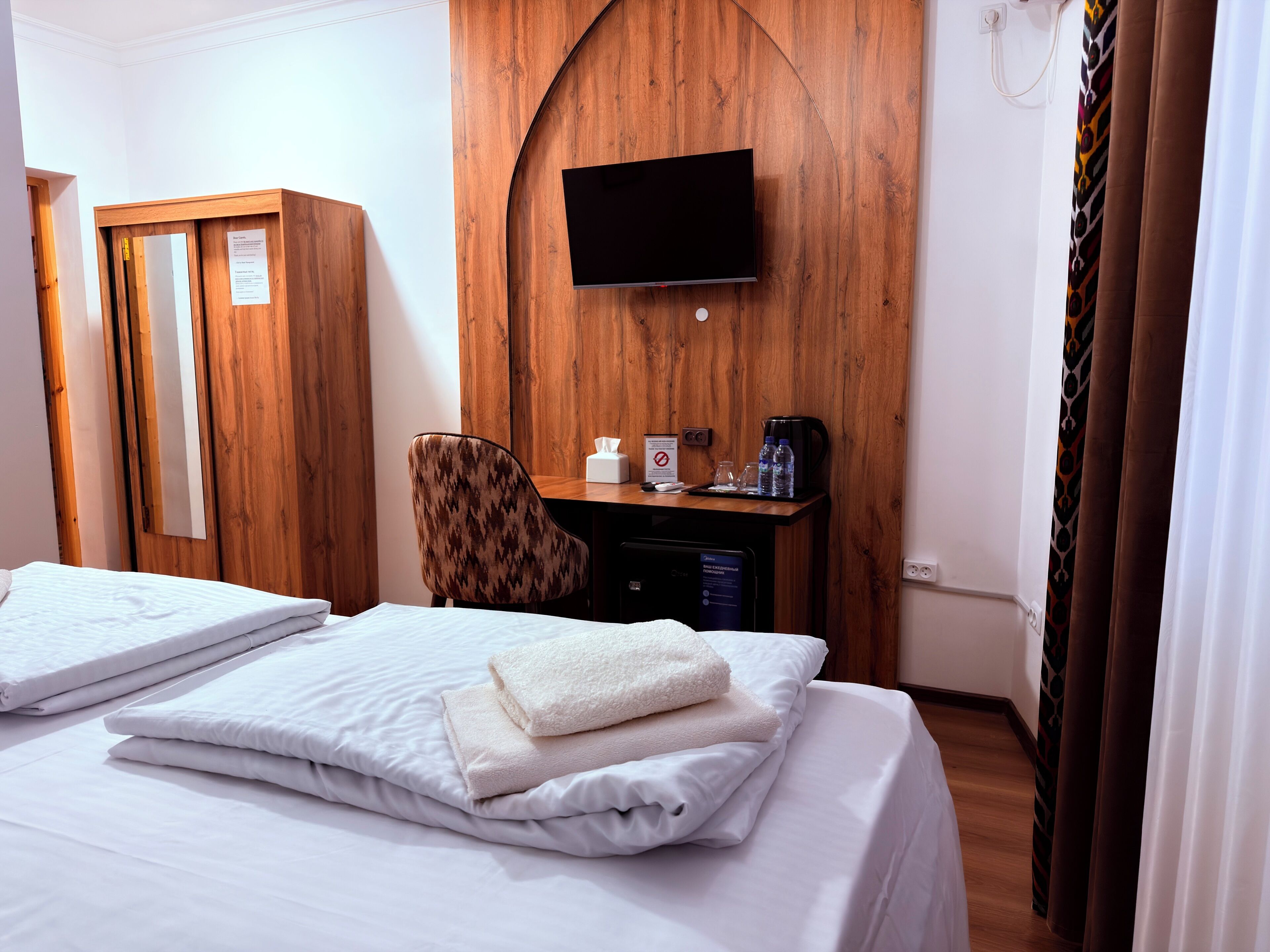Quarto de hotel com cama, escrivaninha com televisão, uma cadeira e um guarda-roupa.