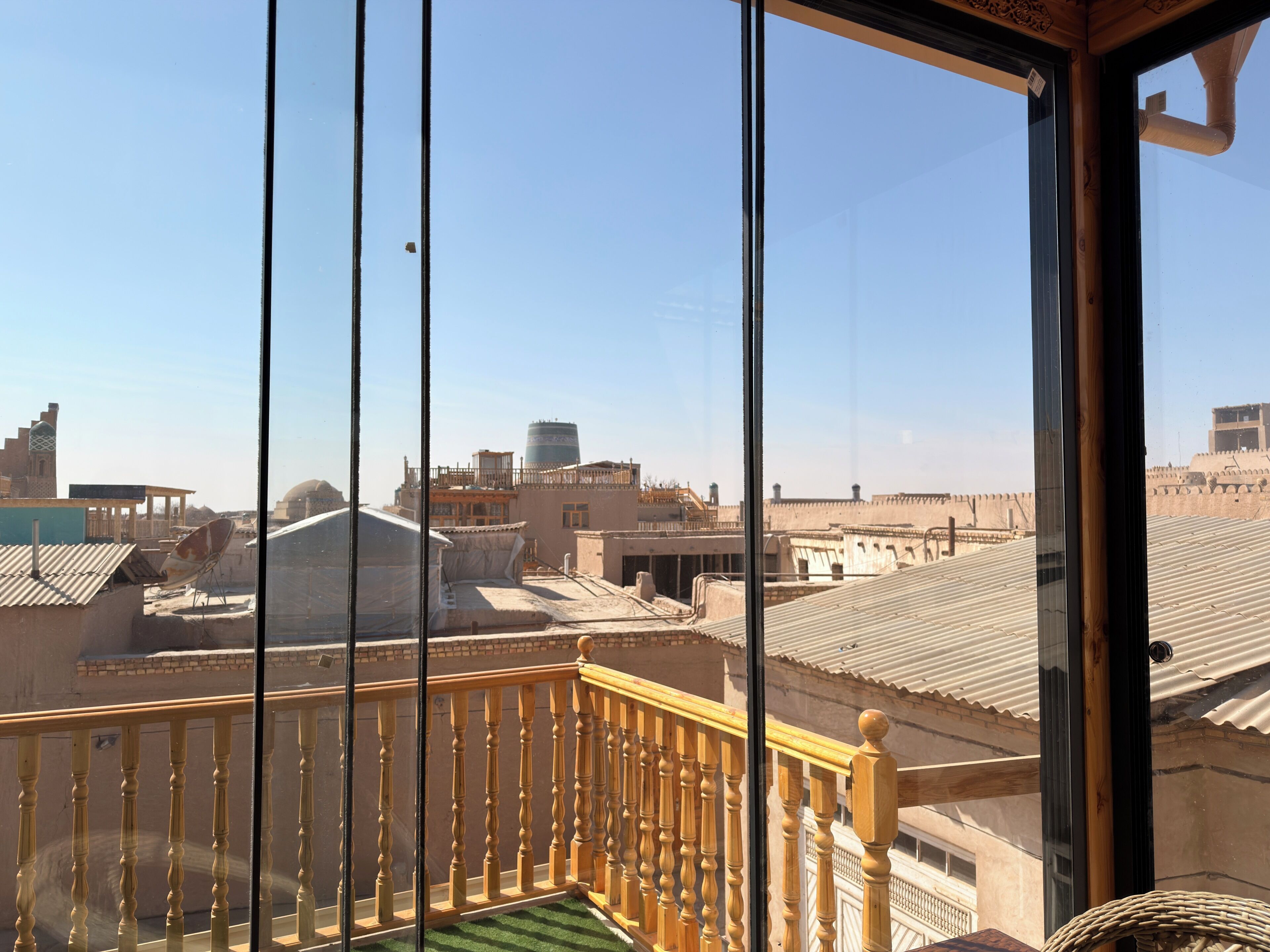 A balcony with a wooden railing, a view of a cityscape with buildings and a water tower, and a clear sky.