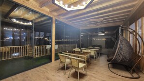 A cozy indoor dining area with wicker furniture, a glass partition, and a hanging chair. - Ulli Oy Boutique Hotel & Terrace (Khiva)