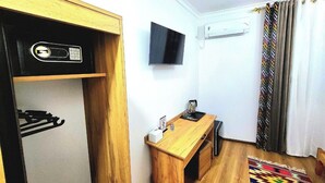 A compact room with a wooden desk, a flat-screen TV, a small kitchenette with a stove, and a patterned rug. - Ulli Oy Boutique Hotel & Terrace (Khiva)