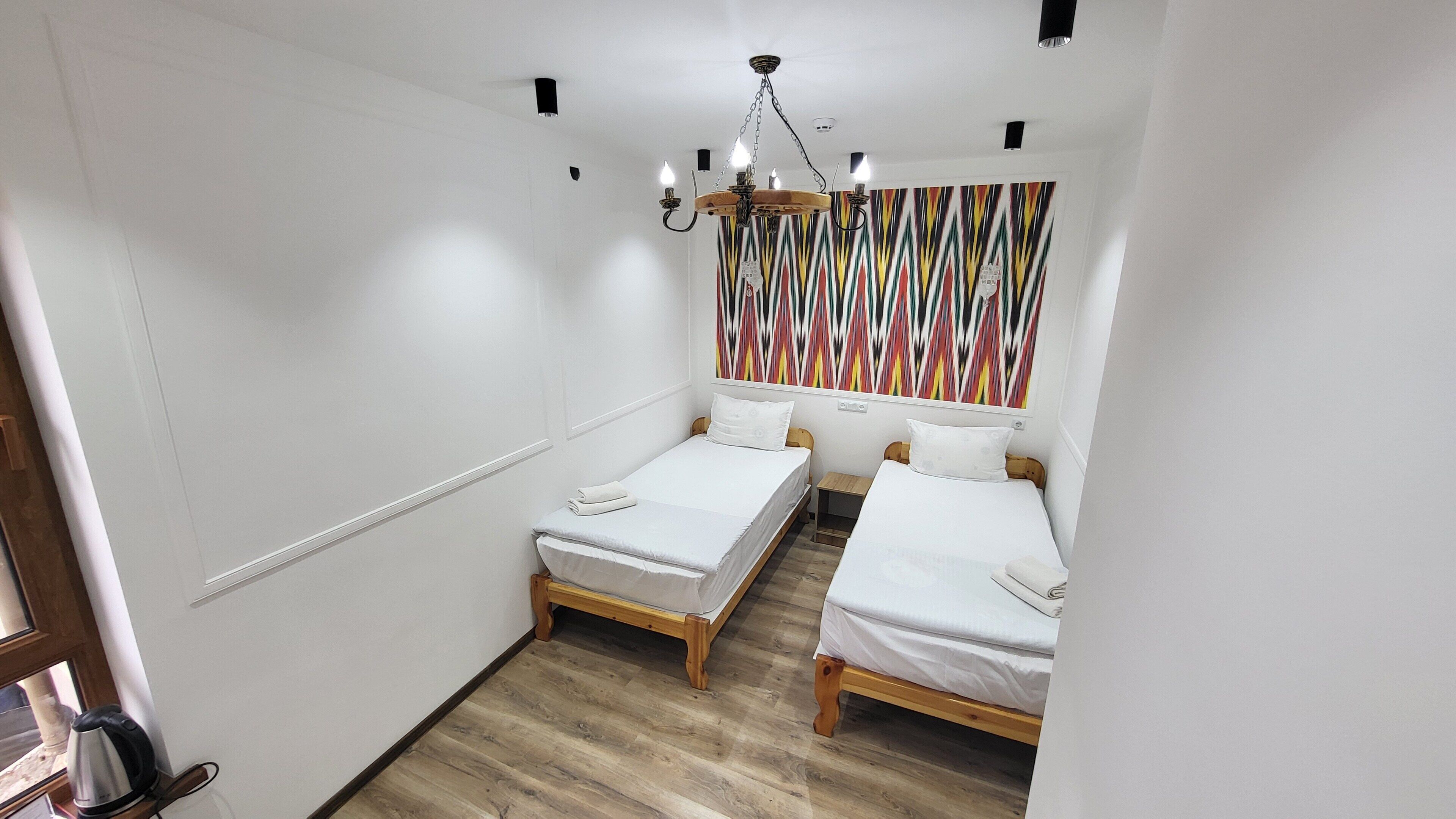 A small, clean room with two single beds, a wooden floor, and a colorful abstract wall art.