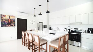 Una cocina moderna con armarios blancos, una isla central con sillas, una estufa negra e iluminación colgante.