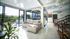 Amplia sala de estar con un sofá seccional beige grande, una mesa de comedor con sillas y una escalera.