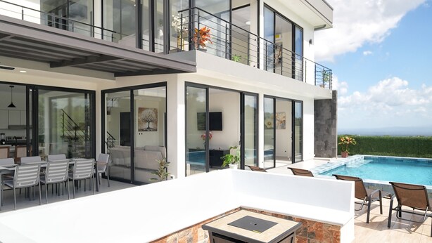 Una casa moderna de dos pisos con un amplio patio, piscina y vista al océano.