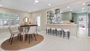 A modern kitchen with a central island, bar stools, and a dining area with a round rug.