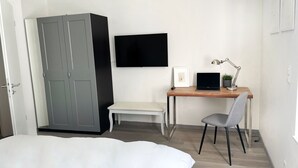 A bedroom with a bed, a desk with a laptop, a chair, a bench, and a wardrobe. - Apartment in guter Lage zur Innenstadt (Dortmund)