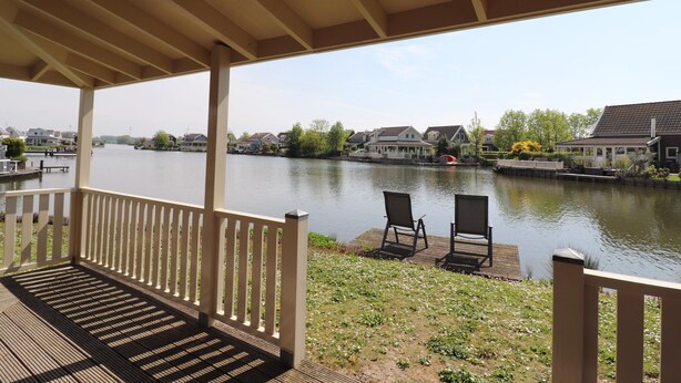 A covered deck with two chairs facing a calm river, surrounded by residential houses. - Bungalow by Water Near Rotterdam and Zeeland (Simonshaven)