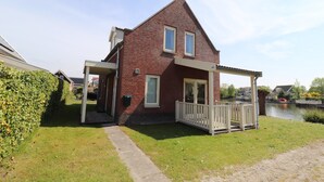 A red brick house with a covered porch, a small garden, and a canal in the background. - Bungalow by Water Near Rotterdam and Zeeland (Simonshaven)