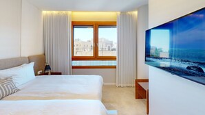 Une chambre d’hôtel avec un grand lit, une table de chevet, une lampe, une fenêtre avec des rideaux et un grand tableau au mur.