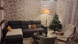 Een gezellige woonkamer met een donkere bank, een klein rond tafeltje, een stoel en een versierde kerstboom.