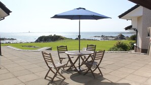 Un patio con tavolo e sedie, un ombrellone blu e vista sul mare.