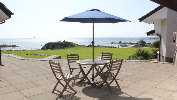 Un patio con una mesa y sillas, una sombrilla azul y vista al mar.