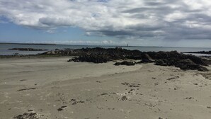 Una playa con formaciones rocosas y un faro distante.