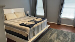 A neatly made bed with a striped bedspread and pillows, a dark blue throw blanket, and folded towels on the bed. - A quiet lakeside home for family, business, or both to relax or be productive. (Virginia Beach)