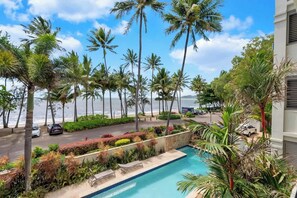 Ein Pool mit Blick auf den Strand, umgeben von Palmen und einer Straße mit Autos.