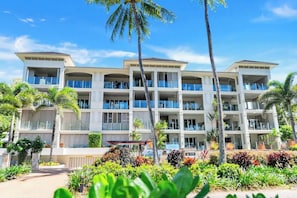 Un hotel a più piani con balconi, palme e un giardino curato.