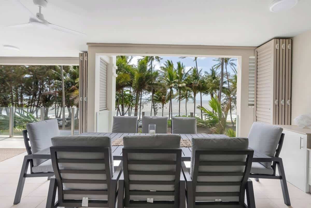 Un espace de restauration moderne avec une table et des chaises, de grandes fenêtres offrant une vue sur les palmiers et l’océan.
