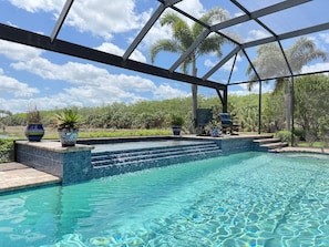 Piscina com água cristalina, rodeada por uma área coberta com escadas que dão acesso à água, plantas em vasos e vista para o exterior.