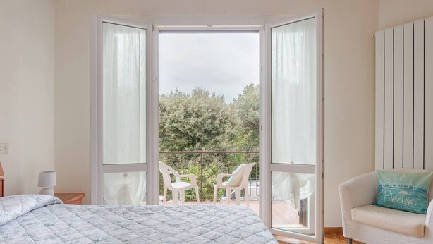 Une chambre à coucher comprenant un lit, une chaise, une table de chevet et une vue sur l’extérieur grâce à une porte coulissante.