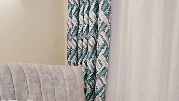 Una cama bien hecha con un plaid gris de punto, almohadas blancas y una almohada decorativa marrón.